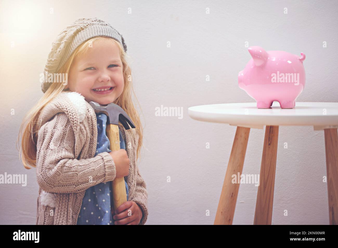 Estoy a punto de ser un millonario. Una niña de pie junto a su banco de cerdos con un martillo. Foto de stock