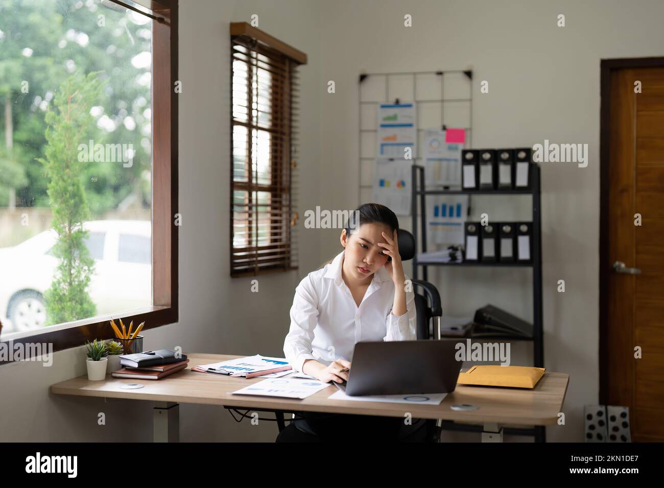 Mujer de negocios asiática cansada con dolor de cabeza en la oficina, sintiéndose enferma en el trabajo. Foto de stock