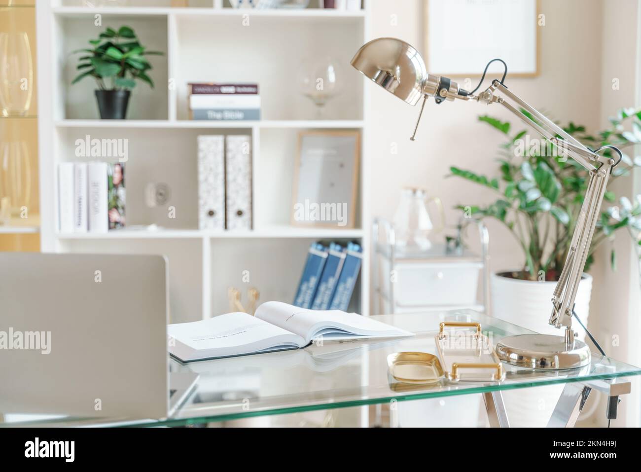 Lugar de trabajo cómodo con un ordenador portátil en la oficina y en casa. Habitación luminosa con grandes ventanas, estantería y planta verde. Trabajo remoto, independiente. Foto de stock