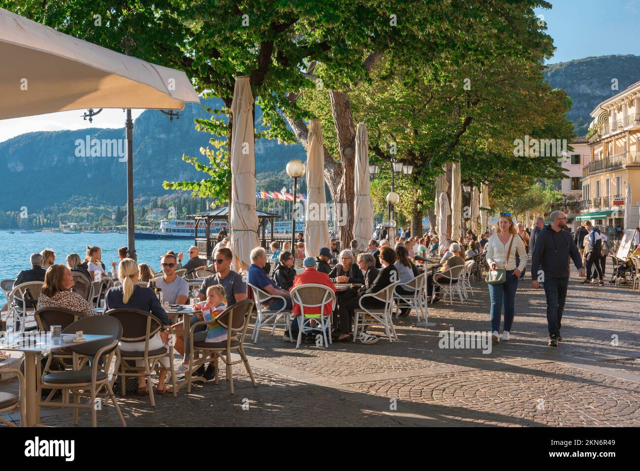 Lago de Garda Italia, vista de la gente que se relaja en las mesas de la cafetería situada a lo largo de la orilla del mar en la pintoresca zona de la ciudad antigua de Garda, Lago de Garda, Véneto Foto de stock