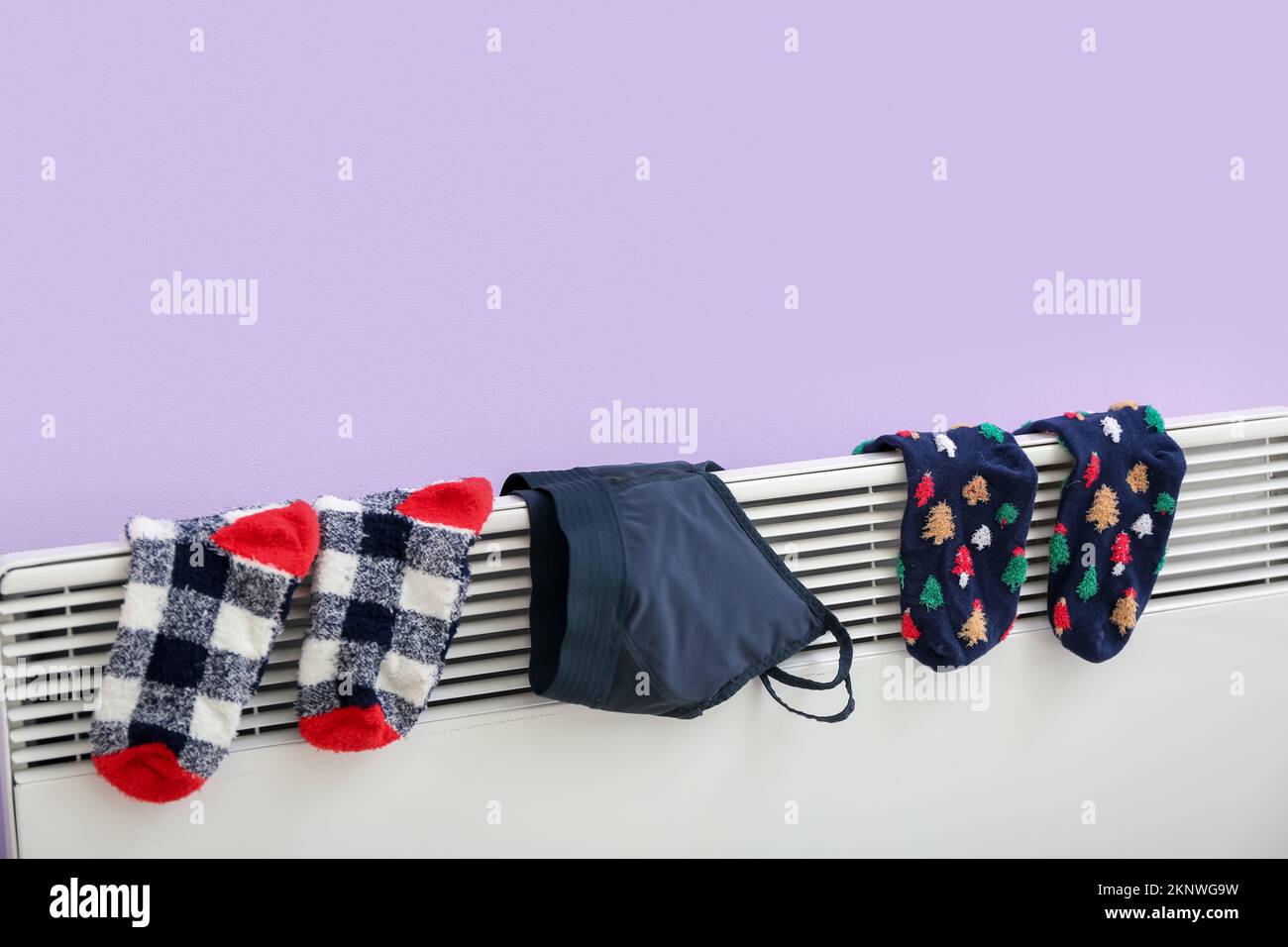 Calcetines cálidos y sujetador deportivo que secan en radiador eléctrico  cerca de la pared lila Fotografía de stock - Alamy