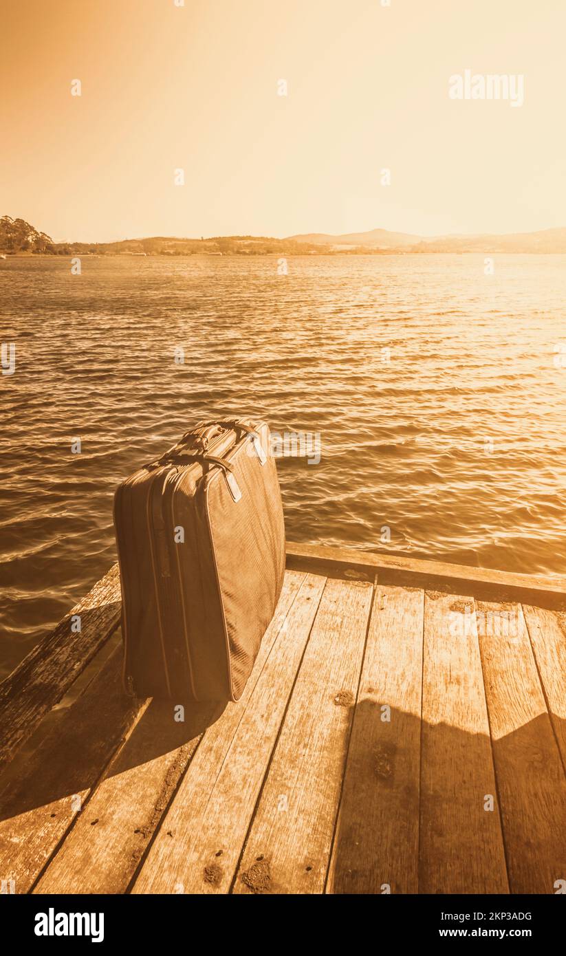 Antigua fotografía manchada y descolorida de un maletín de transporte de equipaje retro sentado al sol de la tarde en el muelle de recogida de cruceros. Aventuras en el extranjero Foto de stock