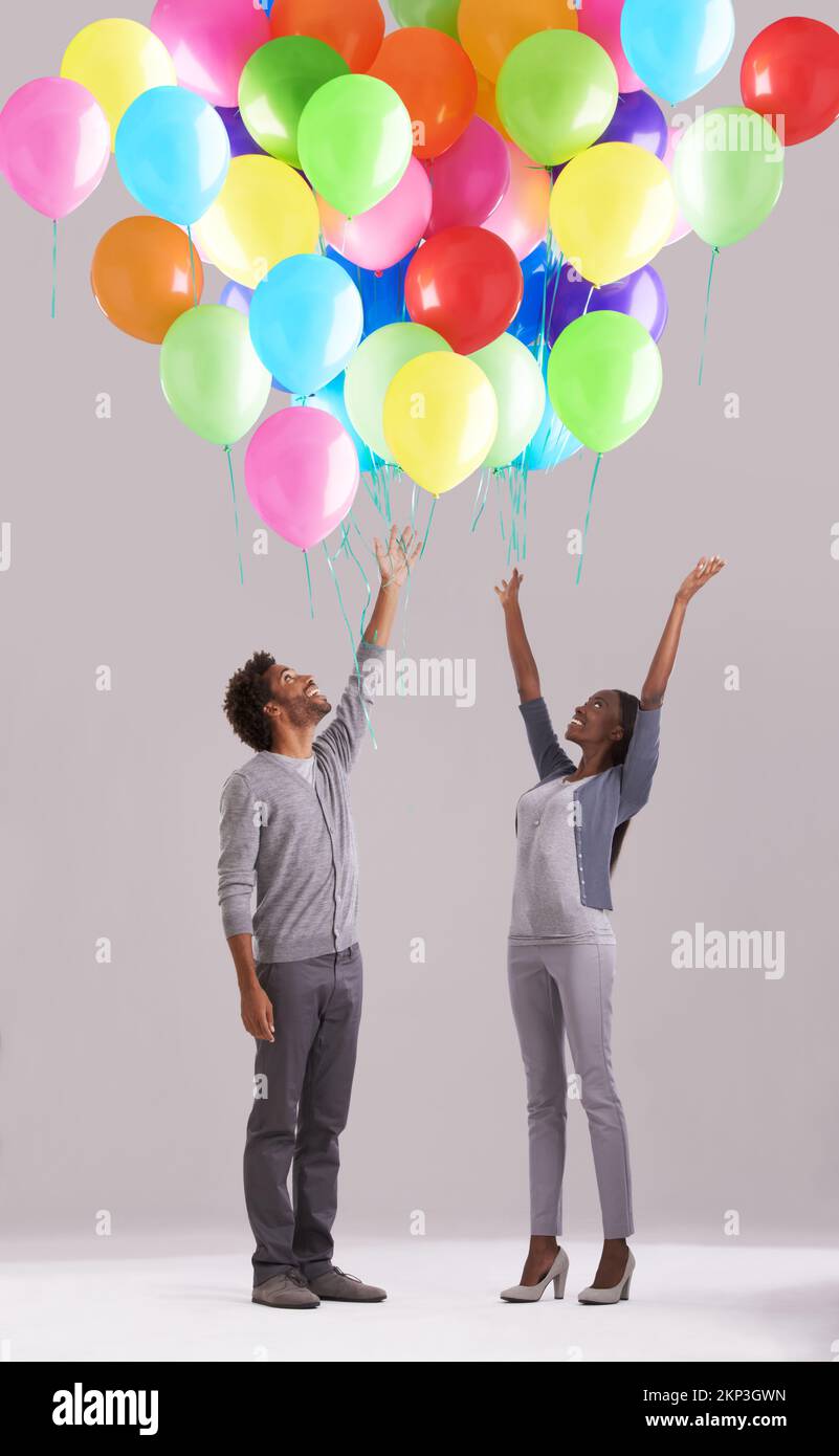 Deje que sus sueños tomen vuelo. Estudio de una joven pareja liberando un montón de globos en el aire. Foto de stock