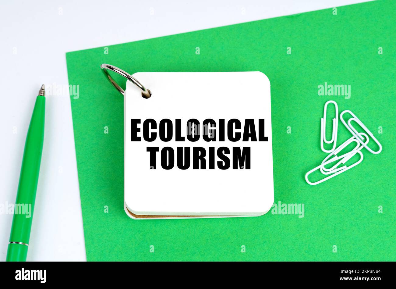 Ecología y concepto industrial. Sobre una superficie blanca se encuentra una hoja de papel verde, una pluma y un cuaderno con la inscripción - Turismo ecológico Foto de stock