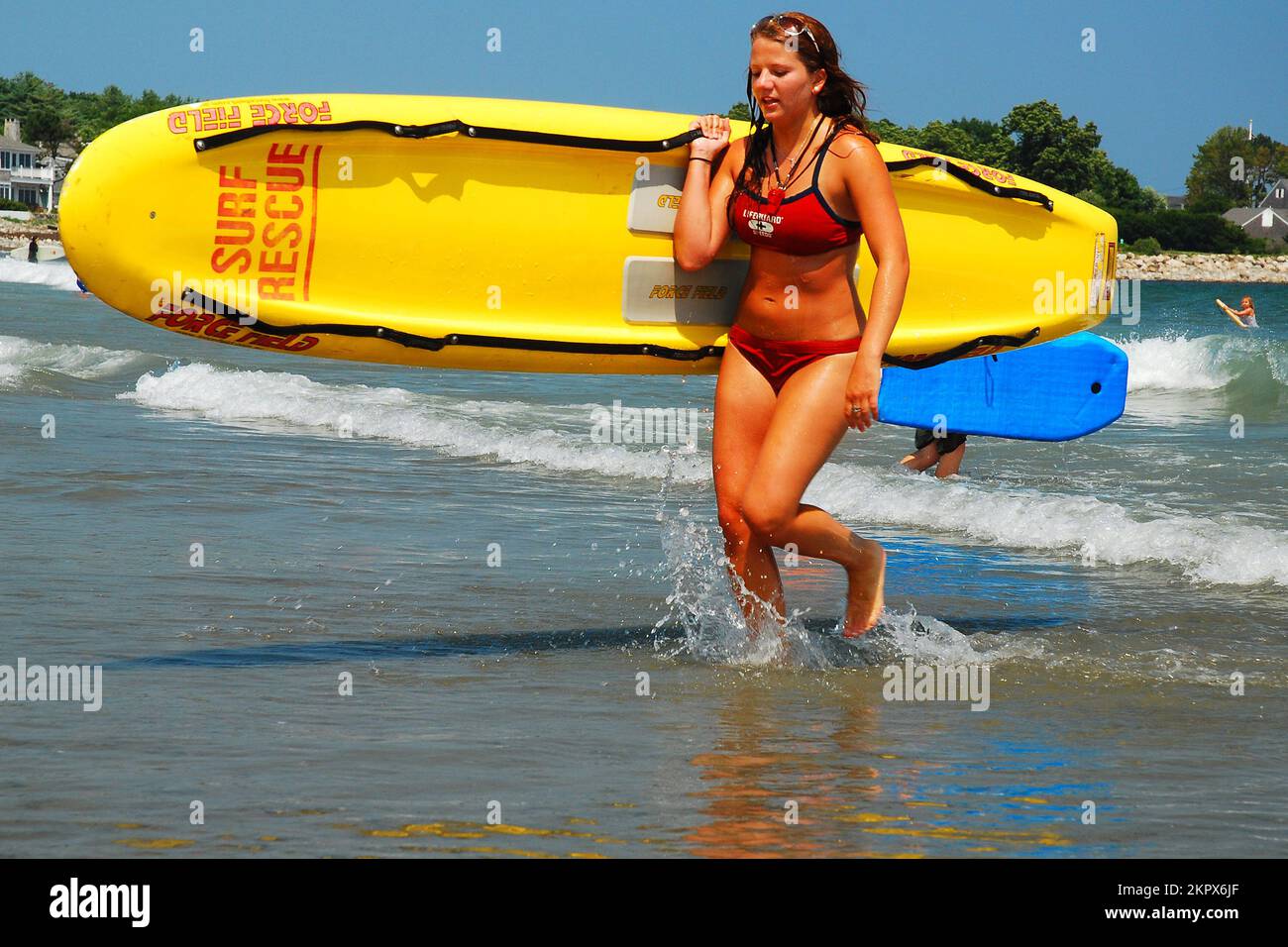 Una socorrista femenina regresa a la costa llevando una balsa que salva la vida al final de sus ejercicios de entrenamiento como parte de su trabajo de verano Foto de stock