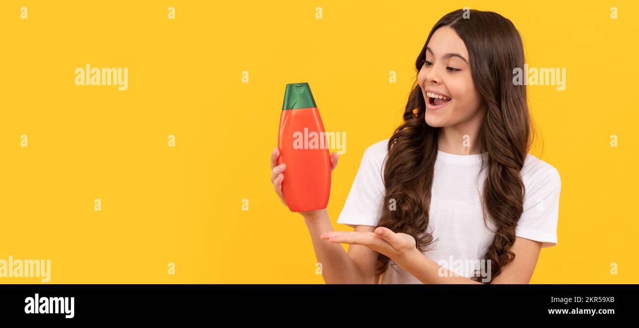 niño feliz con el pelo largo que presenta el producto de la botella del champú, la propuesta del producto. Banner de cuidado de cabello niña, estudio de cabecera póster con espacio de copia. Foto de stock