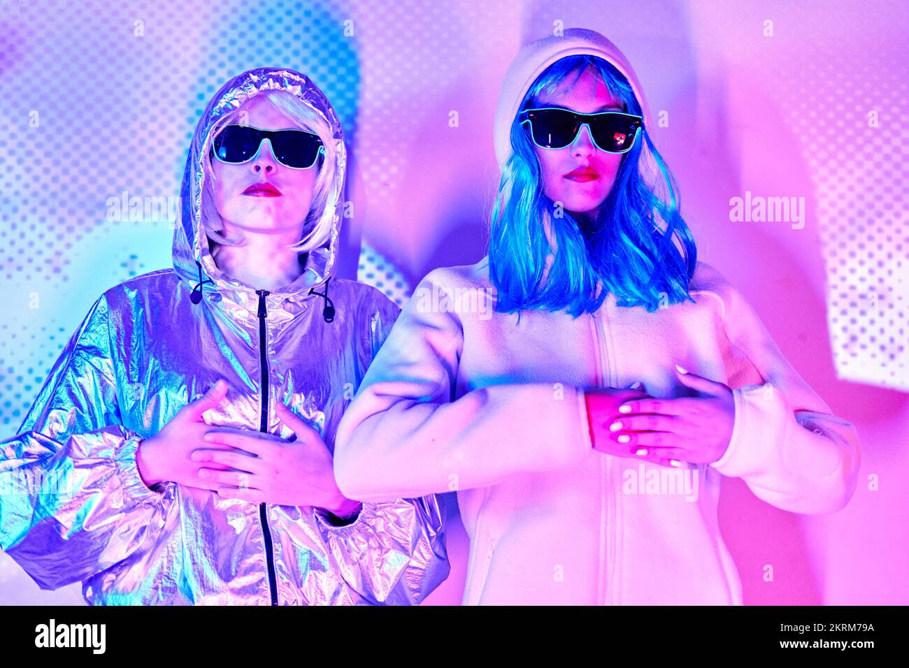 Mujeres sin emociones con ropa cyberpunk y capuchas sobre la cabeza contra  la brillante iluminación púrpura de neón en el estudio con los dedos juntos  Fotografía de stock - Alamy