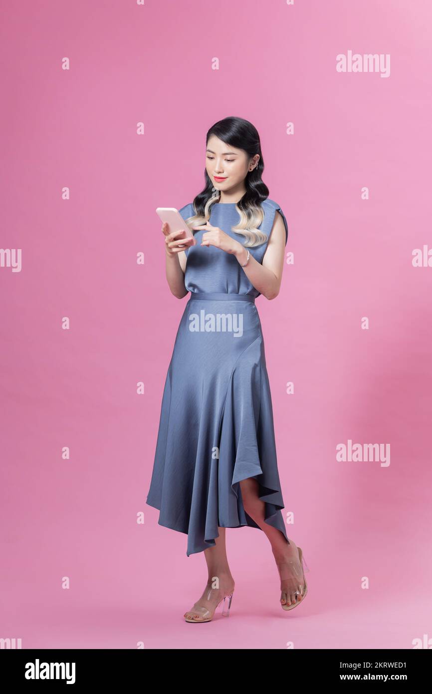 Bonita mujer sosteniendo smartphone y navegando por Internet o charlando aislado sobre fondo rosa en el estudio Foto de stock