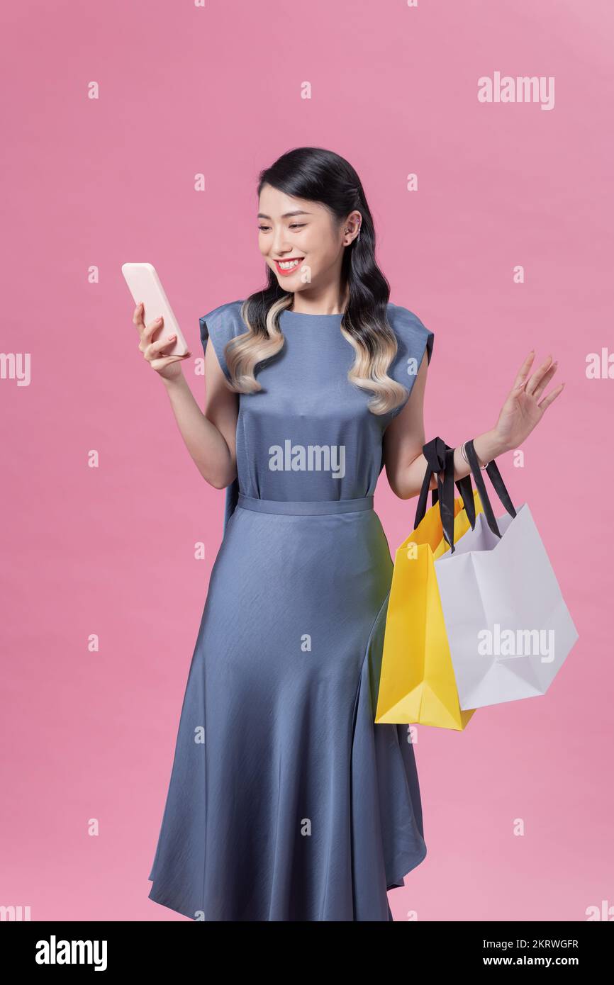 Hermosa joven feliz mujer asiática con una bolsa de compras de colores utilizando un teléfono para hacer compras en línea. Sorprendido por grandes descuentos Foto de stock