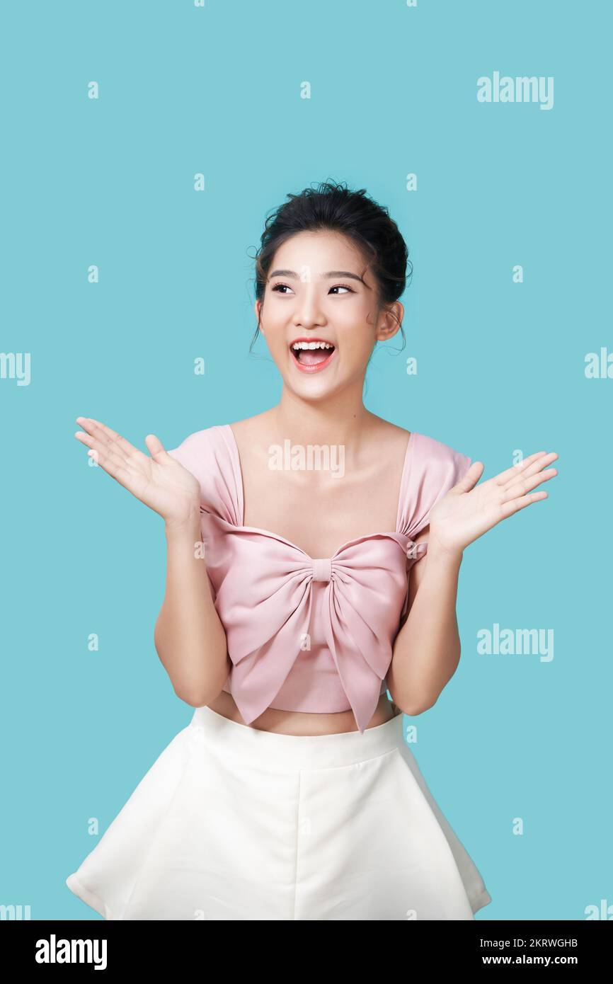 La modelo femenina asiática de aspecto agradable sonríe alegremente, extiende las palmas cerca de la cara, expresa emociones positivas aisladas sobre fondo cian Foto de stock