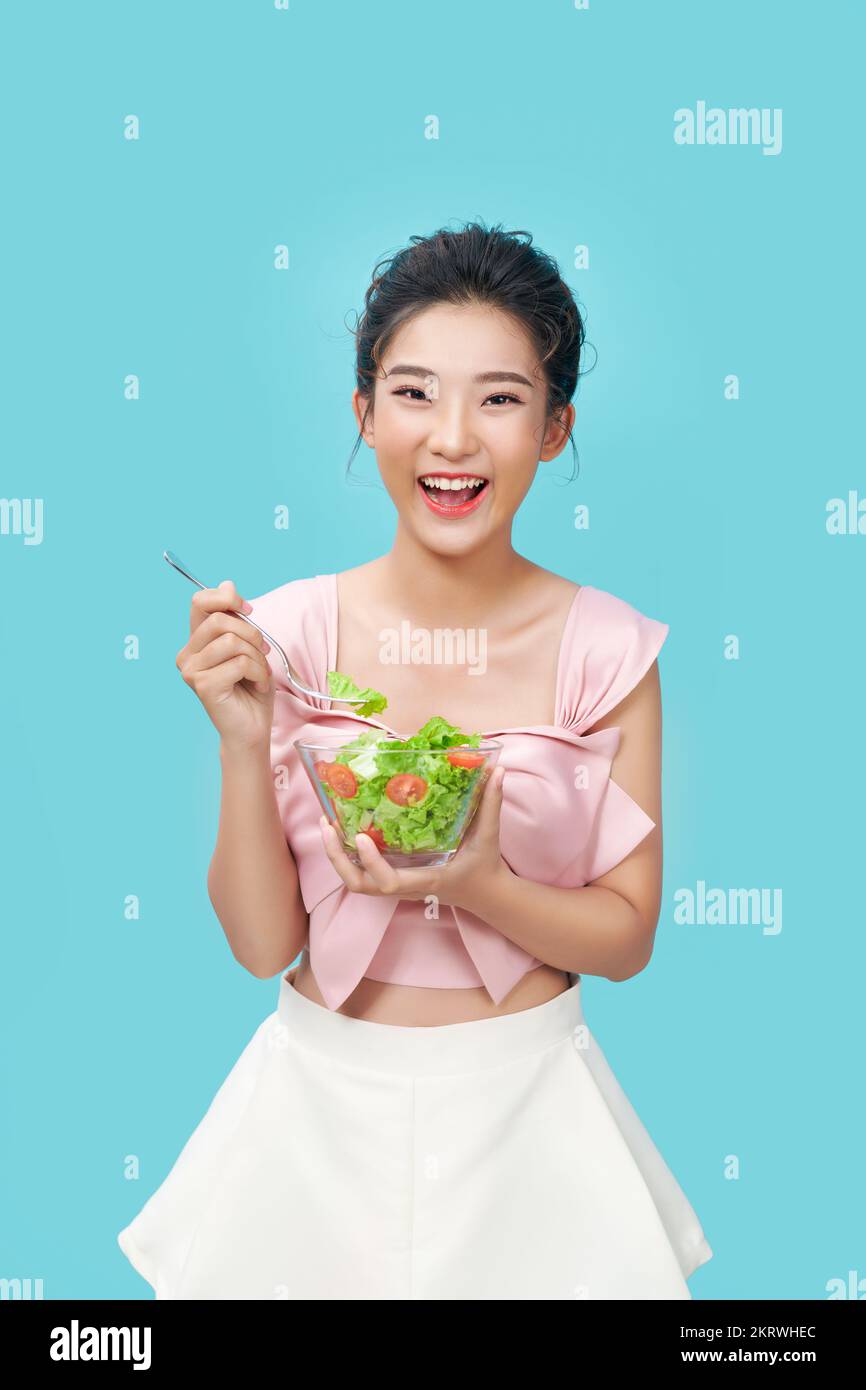 Mujer joven asiática Eatiing ensalada sobre fondo azul dieta concepto de alimentos Foto de stock