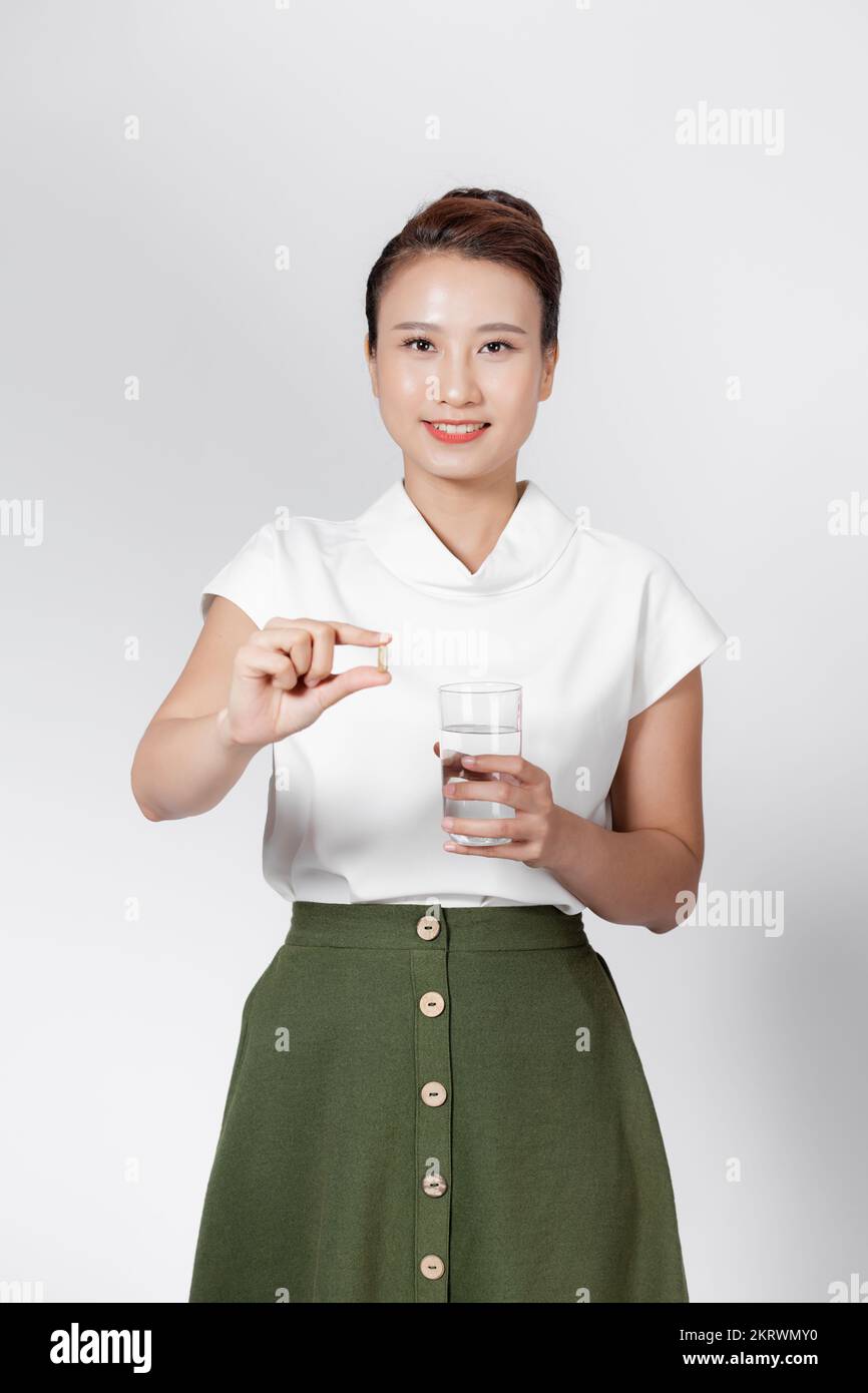 Mujer joven asiática que sostiene la cápsula del suplemento y un vaso de agua Foto de stock