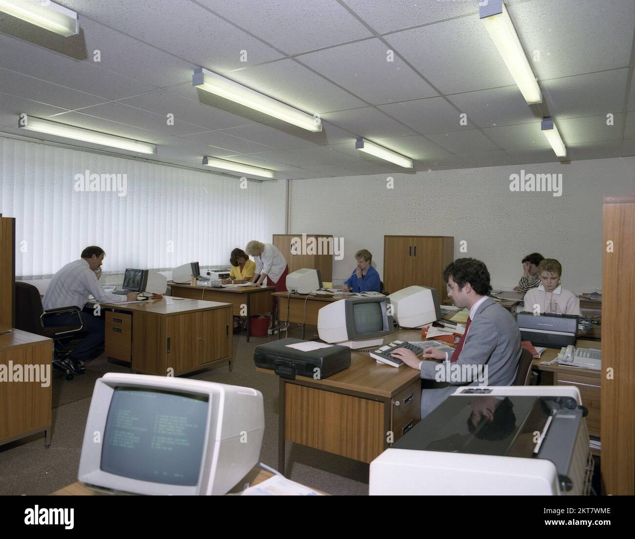1989s, trabajadores de oficina adultos, históricos, sentados en escritorios de madera en una oficina abierta, usando los terminales de computadoras de la época, Inglaterra, Reino Unido. Una de las empleadas está utilizando una máquina de escribir Olympia International. Foto de stock
