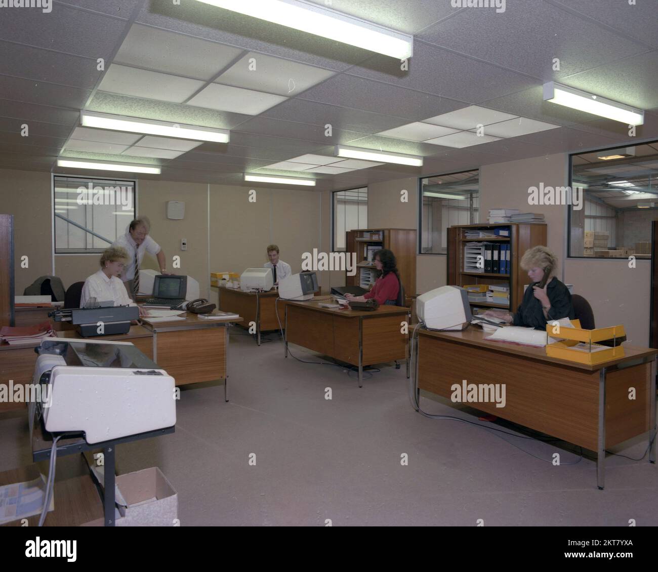1989s, histórico, interior de una oficina de planta abierta, terminal de ordenadores de la época en los escritorios de madera. Una máquina de escribir internacional Olympia que está siendo utilizada por una empleada. Foto de stock