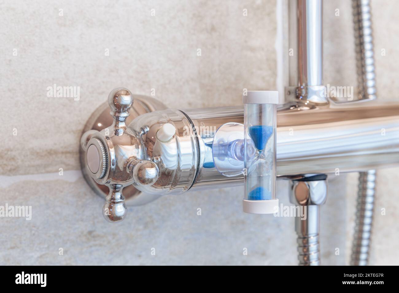 Un grifo de ducha en el cuarto de baño con un reloj de arena adjunto para reducir el tiempo de ducha con el fin de ahorrar agua y energía. Foto de stock