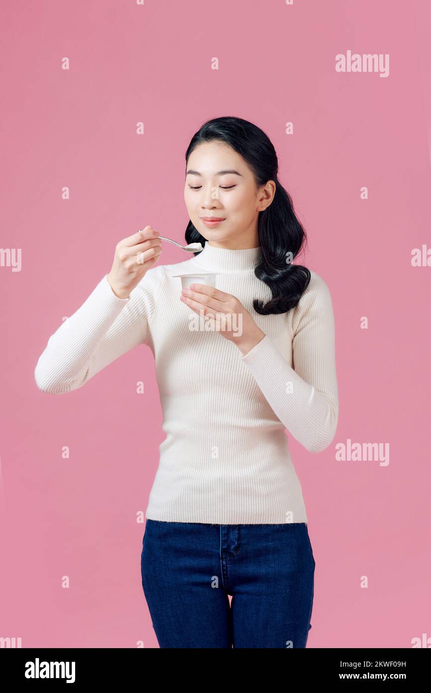 joven hermosa mujer comiendo yogur con cuchara buscando satisfecho estilo de vida saludable aislado fondo rosa Foto de stock