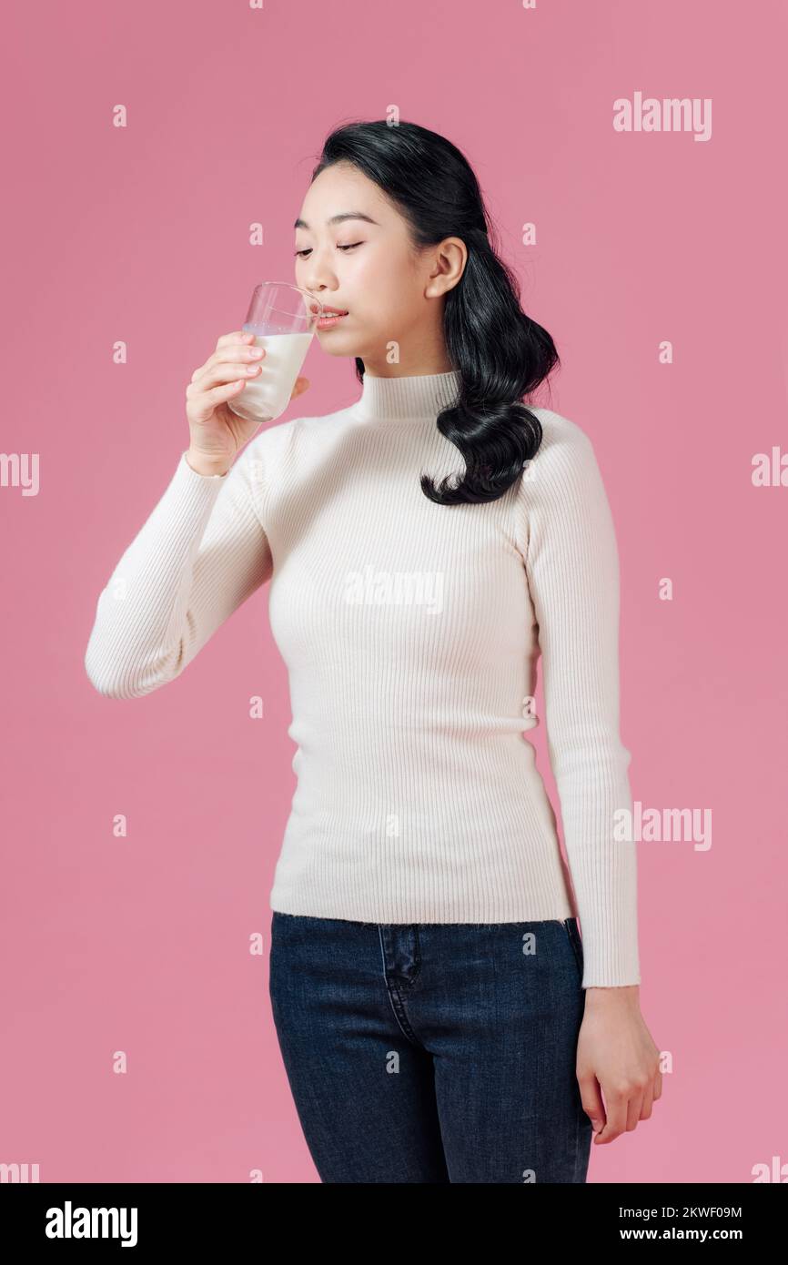 Retrato de una mujer asiática satisfecha bebiendo leche del vaso aislada sobre fondo rosa Foto de stock