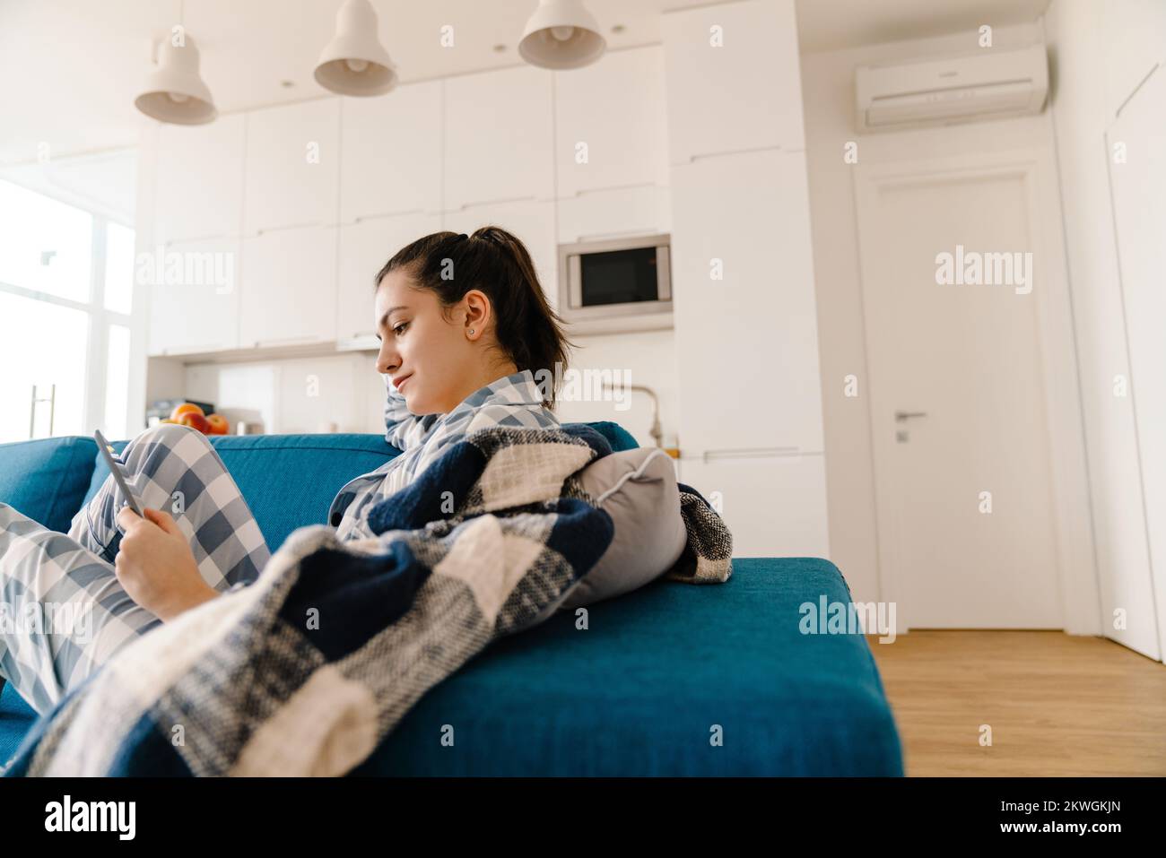 Mujer joven con tablet PC mientras descansa en el sofá en casa Foto de stock