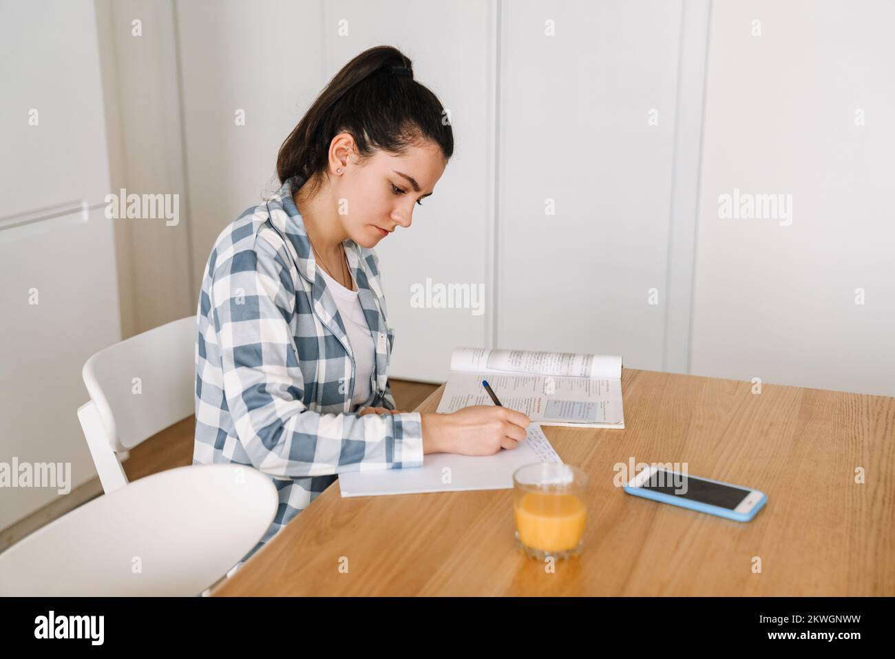 Mujer joven haciendo la tarea mientras se sienta en la mesa de la cocina en casa Foto de stock
