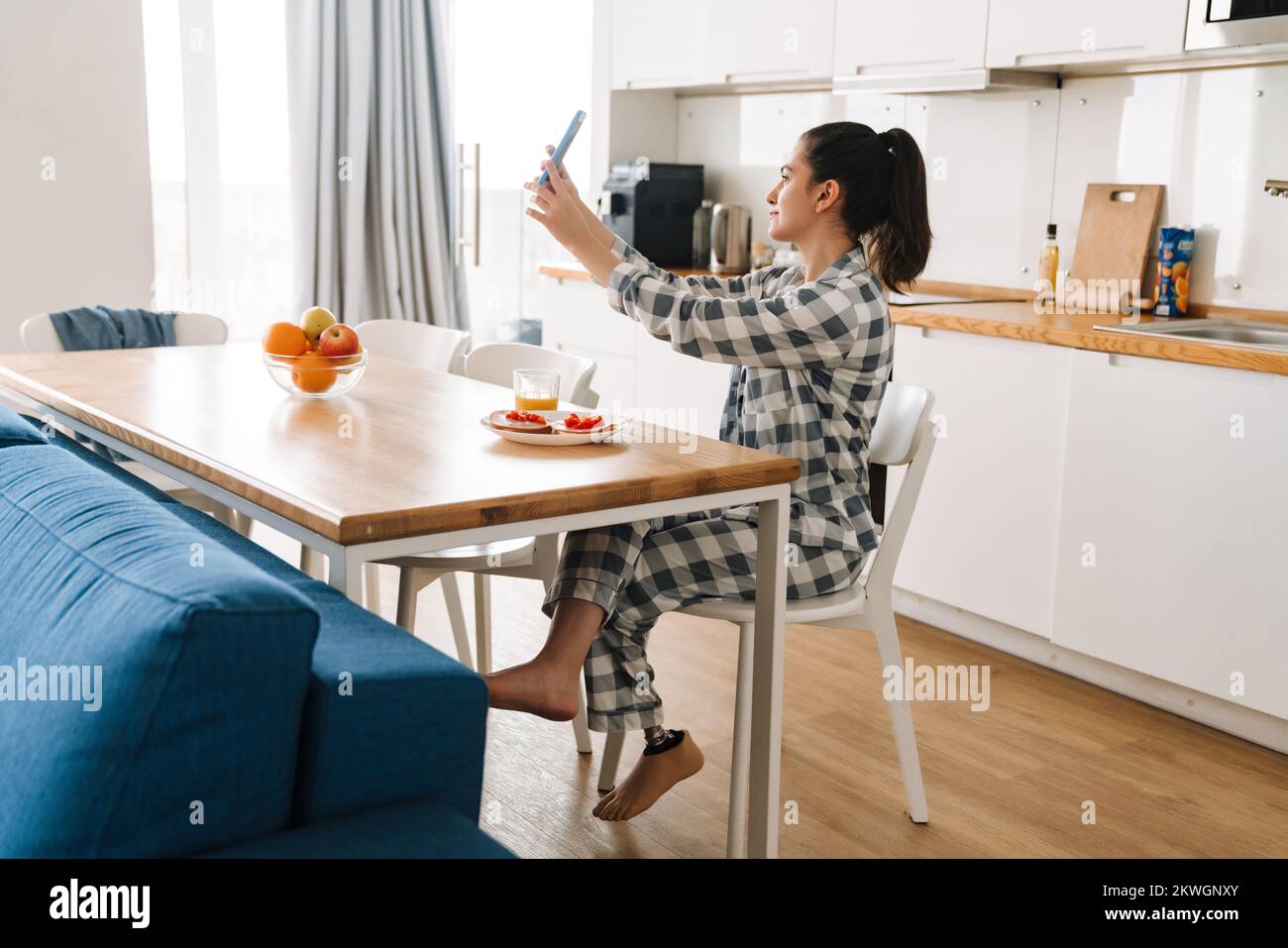 Mujer joven con prótesis tomando una foto de selfie mientras desayuna en casa Foto de stock