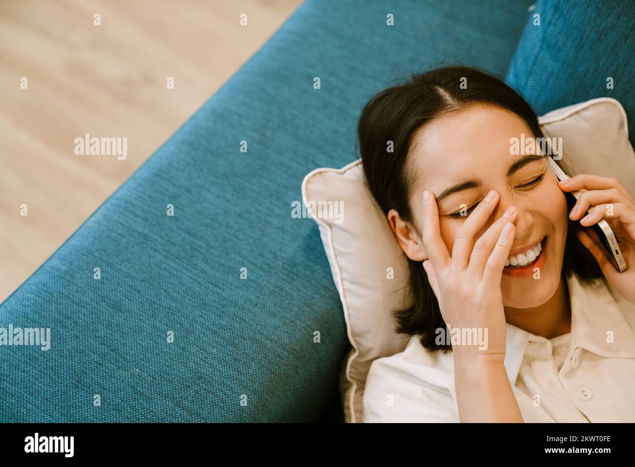 Joven linda riendo chica asiática hablando por teléfono y acostada en el sofá en casa Foto de stock