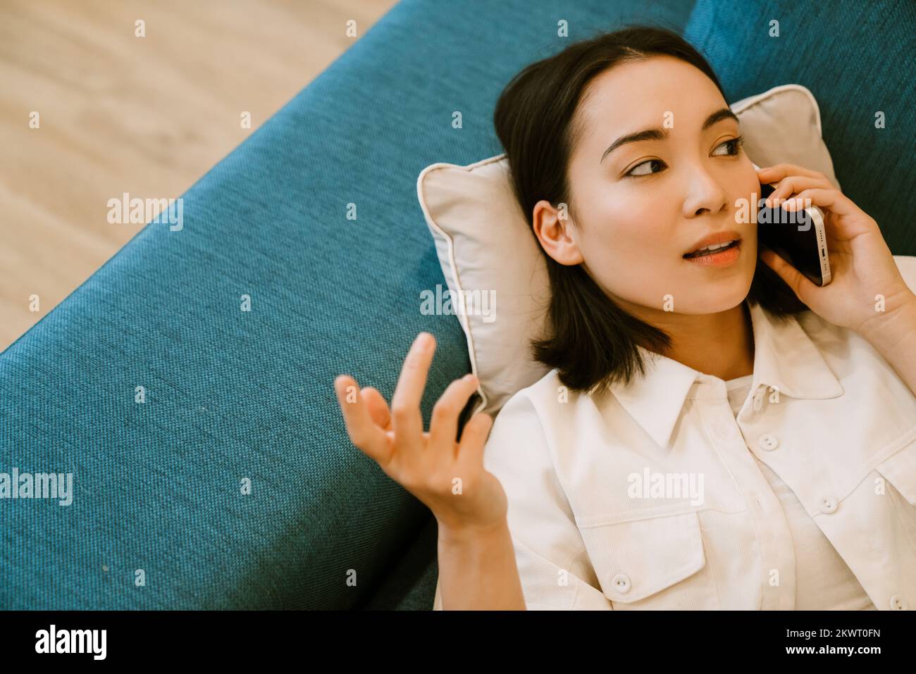 Joven linda chica asiática hablando por teléfono y acostada en el sofá en casa Foto de stock