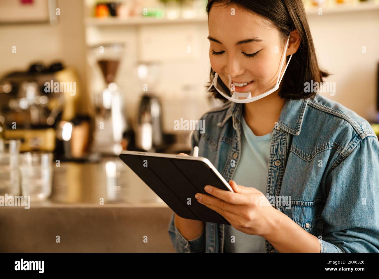Joven camarera asiática sonriendo mientras trabajaba con la tableta en el café Foto de stock