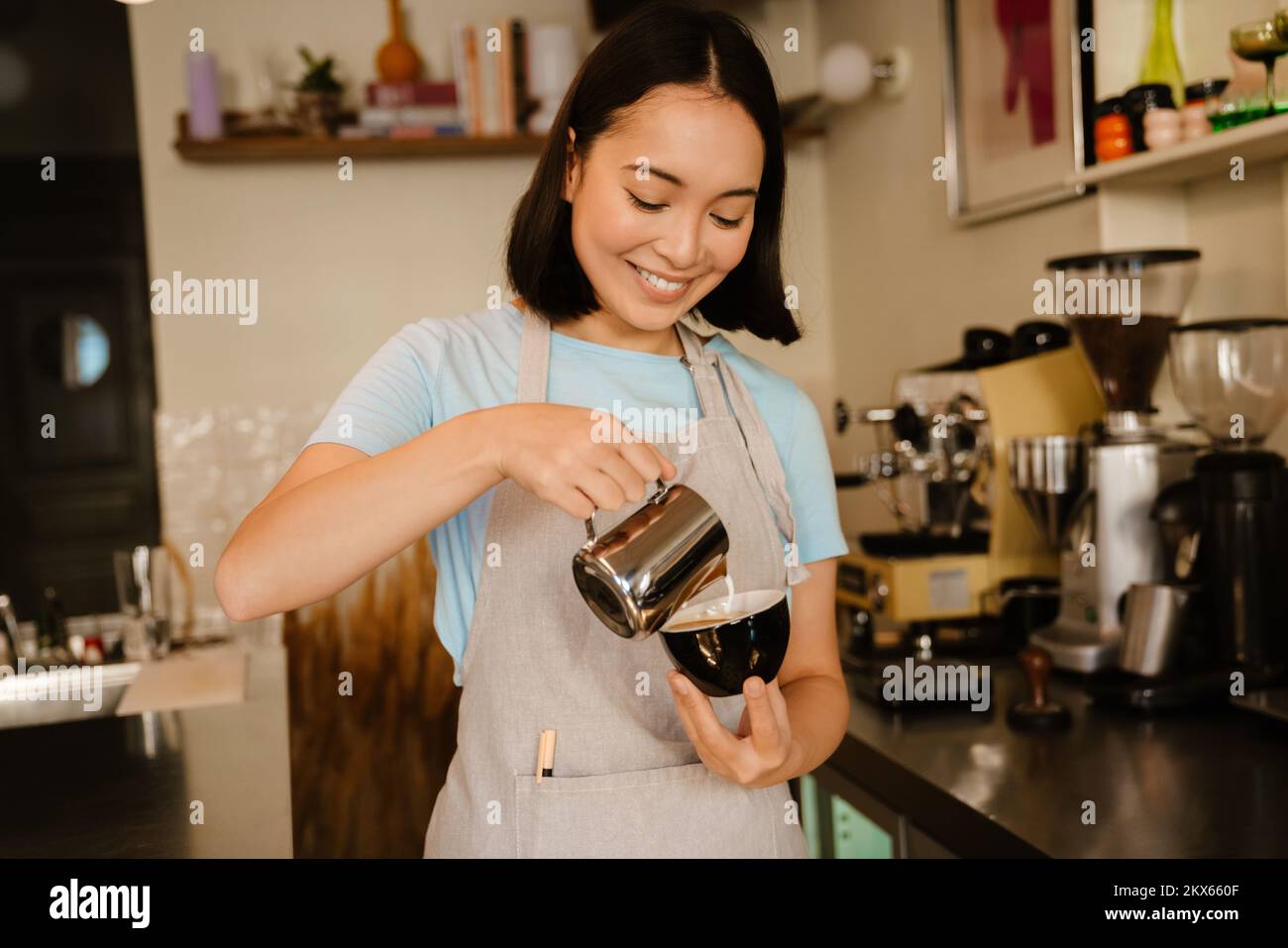 Joven mujer barista asiática con delantal sonriendo mientras hacía café en el café Foto de stock
