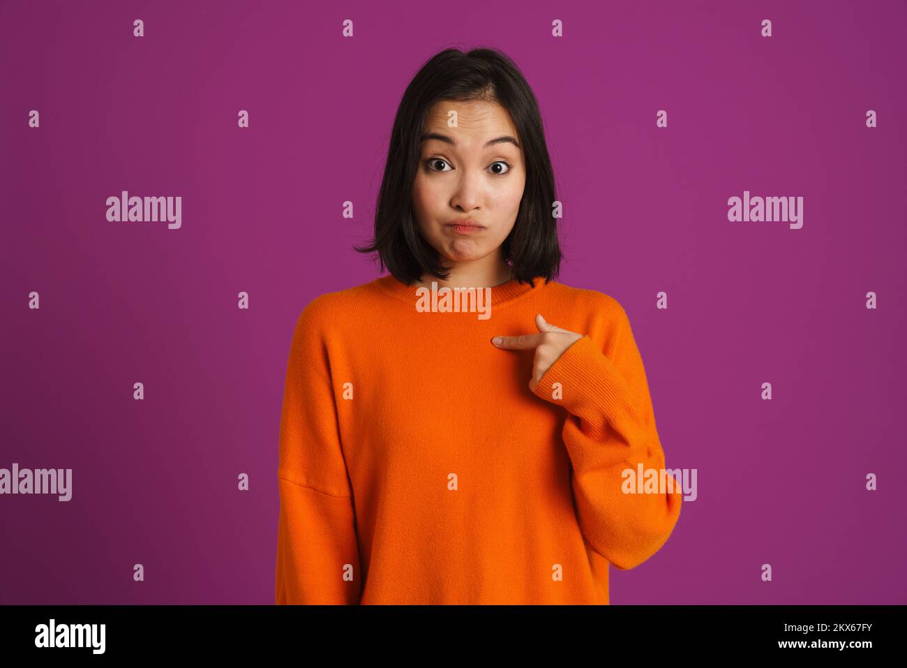 Joven mujer asiática expresando sorpresa y señalando con los dedos a sí misma aislada sobre fondo púrpura Foto de stock
