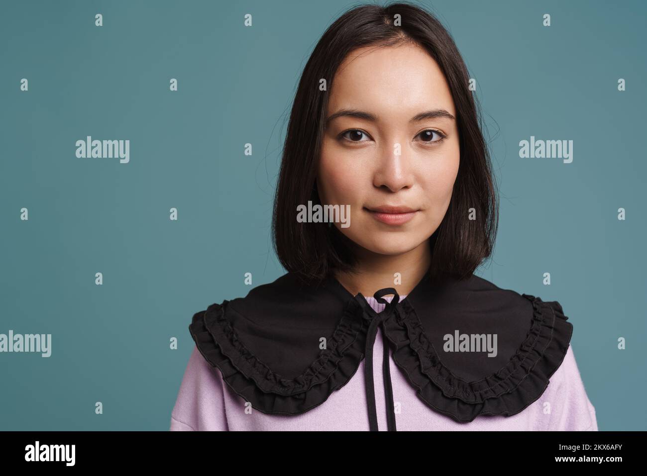 Mujer joven asiática con cuello posando y mirando la cámara aislada sobre fondo azul Foto de stock