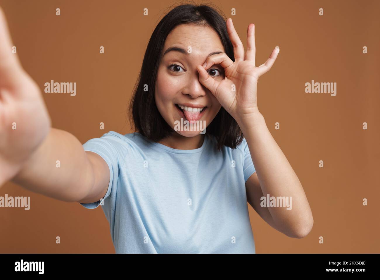 Mujer joven asiática que se divierte mientras toma una foto de selfie aislada sobre fondo beige Foto de stock