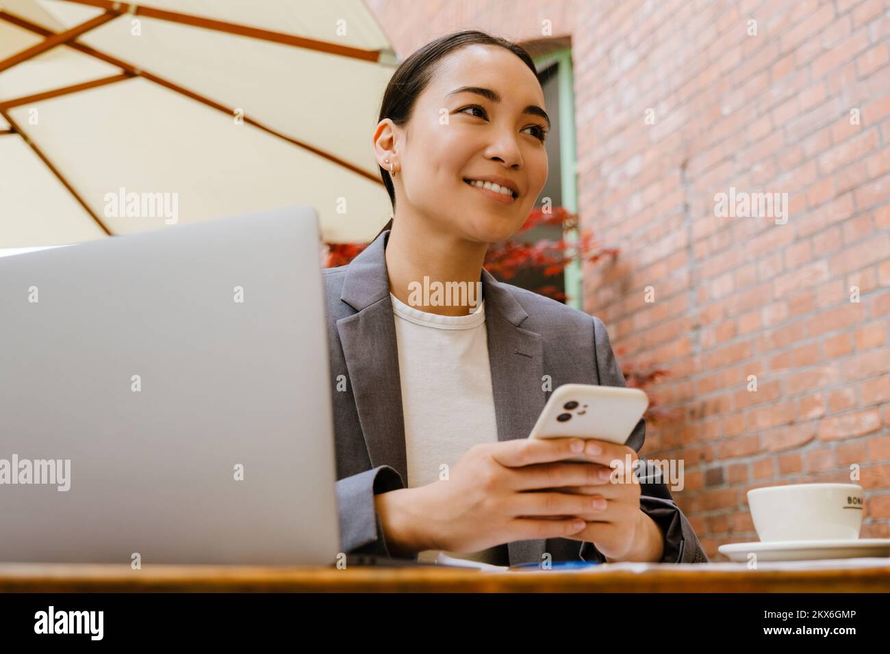 Mujer asiática usando el teléfono móvil mientras trabaja con el ordenador portátil en la cafetería al aire libre Foto de stock