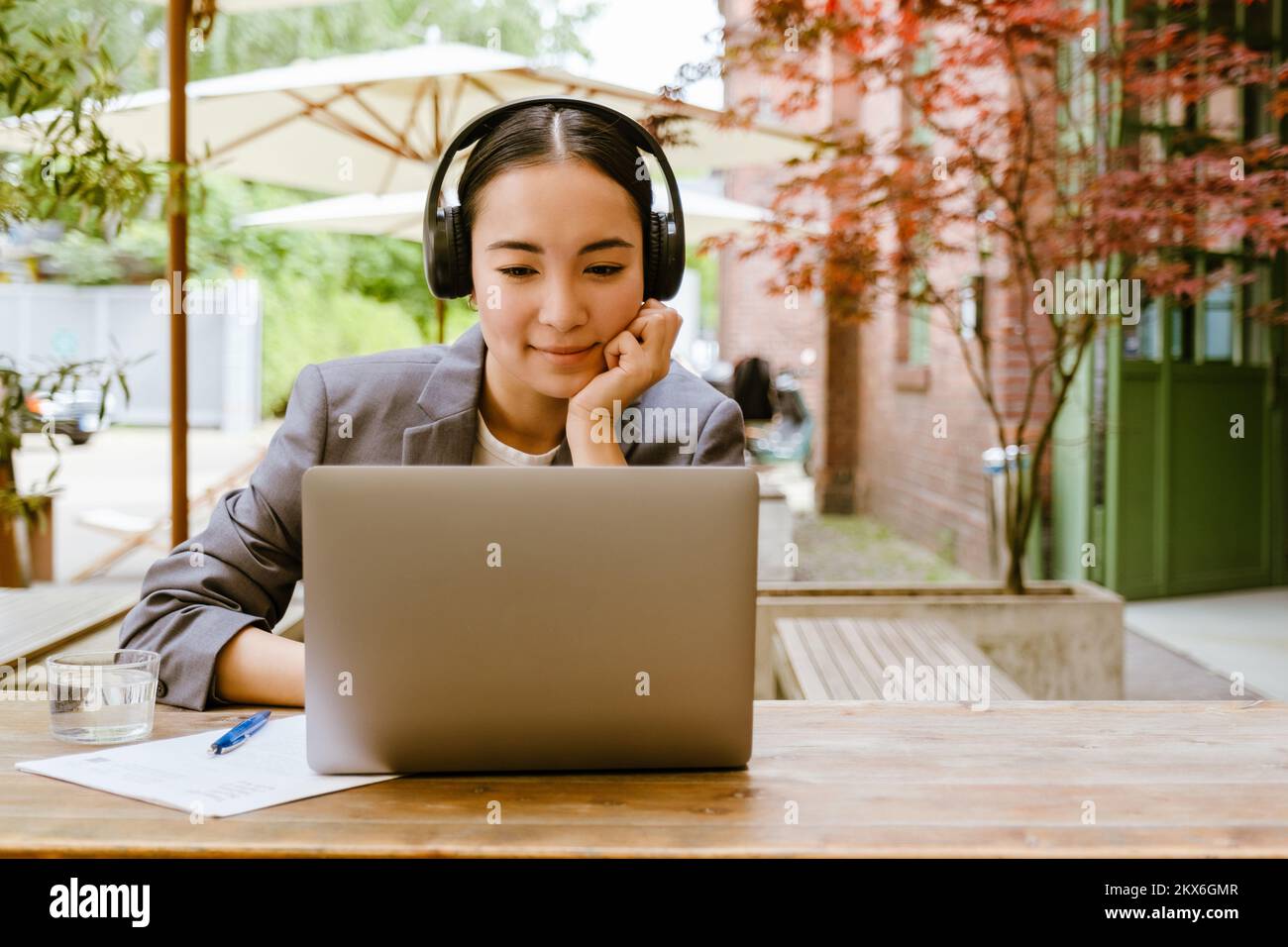 Mujer joven asiática con auriculares trabajando con un portátil mientras se sienta en un café al aire libre Foto de stock