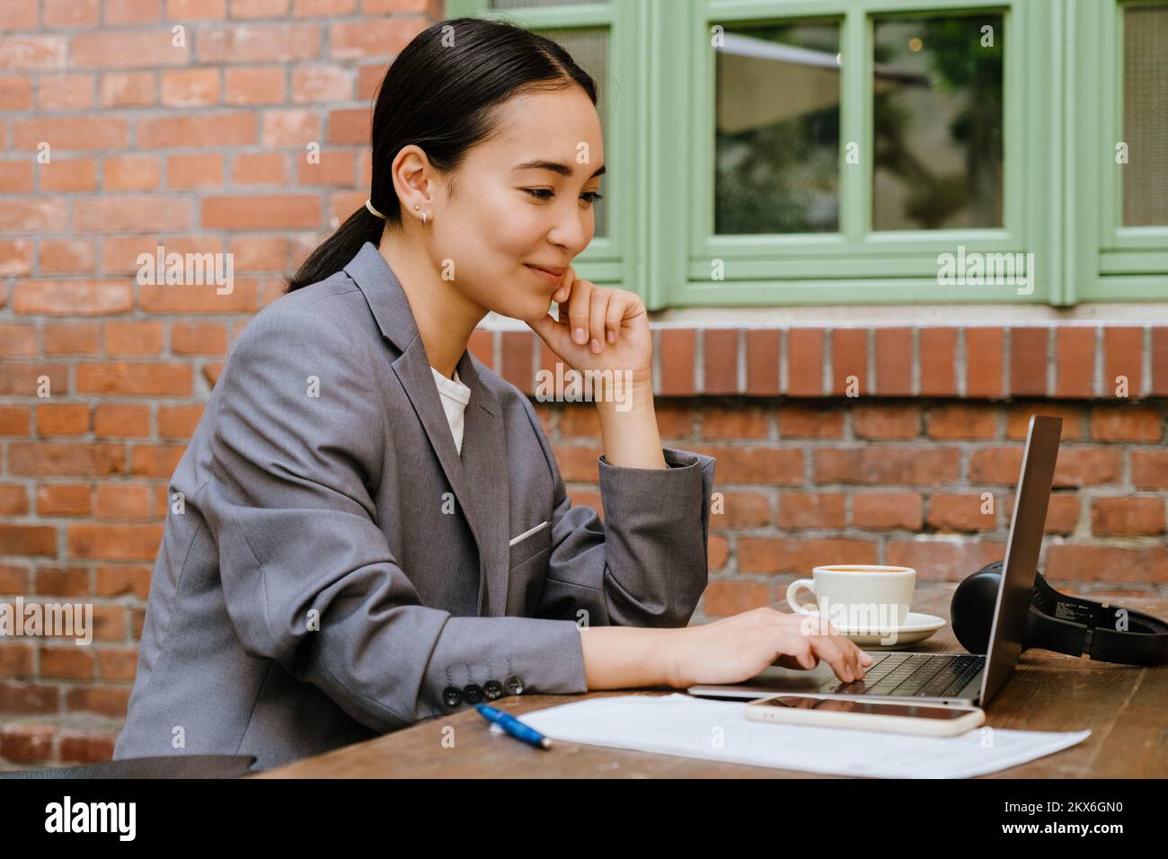 Mujer joven asiática que trabaja con un ordenador portátil mientras está sentada en un café al aire libre Foto de stock