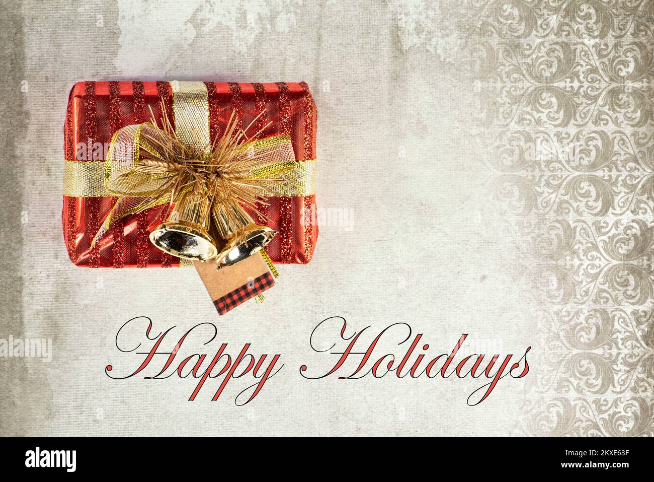 Pequeña caja de regalo envuelta en rojo con cinta y tarjeta de felicitación navideña con campanas y texto 'Happy Holidays'. Foto de stock