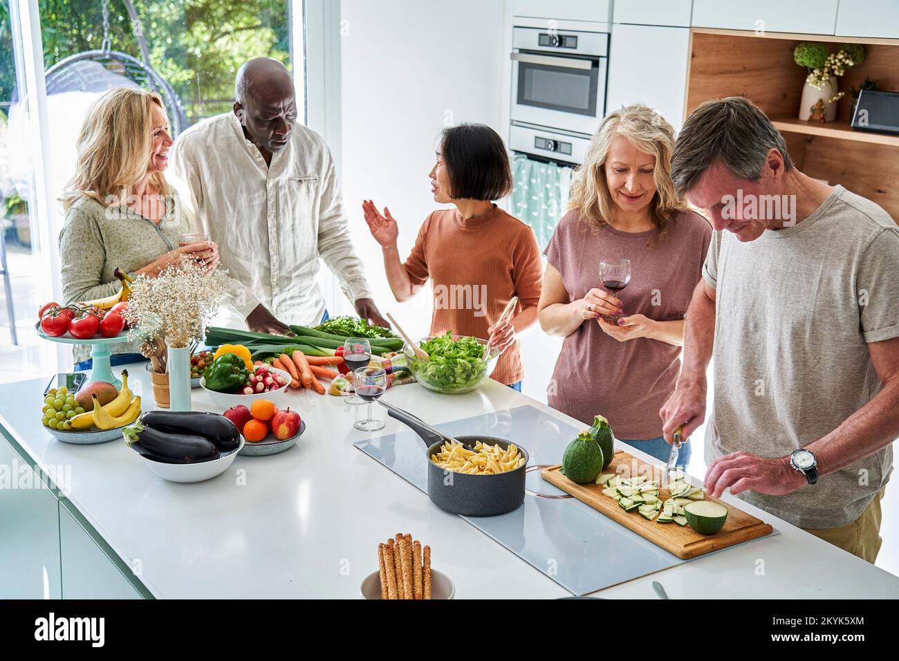 Grupo de amigos mayores se reunieron en la cocina mientras preparaban la cena Foto de stock