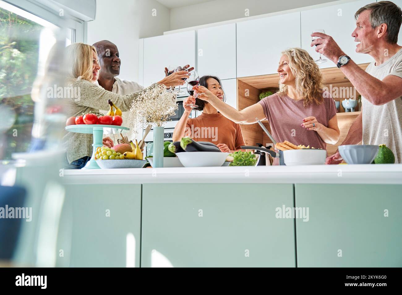 Diverso grupo de amigos mayores brindando mientras se reunían en la cocina Foto de stock
