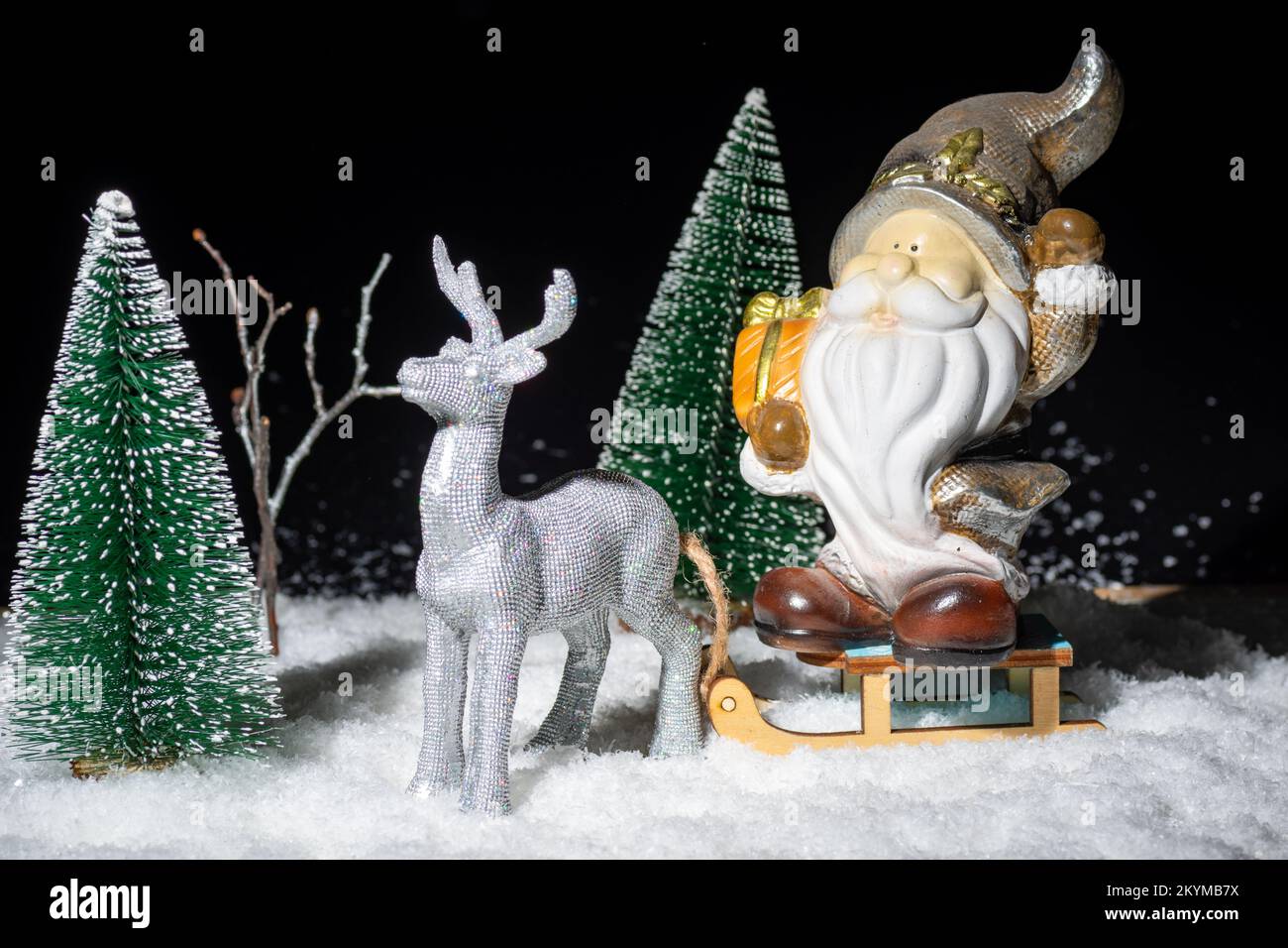 Tarjeta de Navidad con un reno llevando un trineo con Papá Noel con regalos en la nieve entre los abetos por la noche, creativo. Historia de Navidad. Nuevo Foto de stock