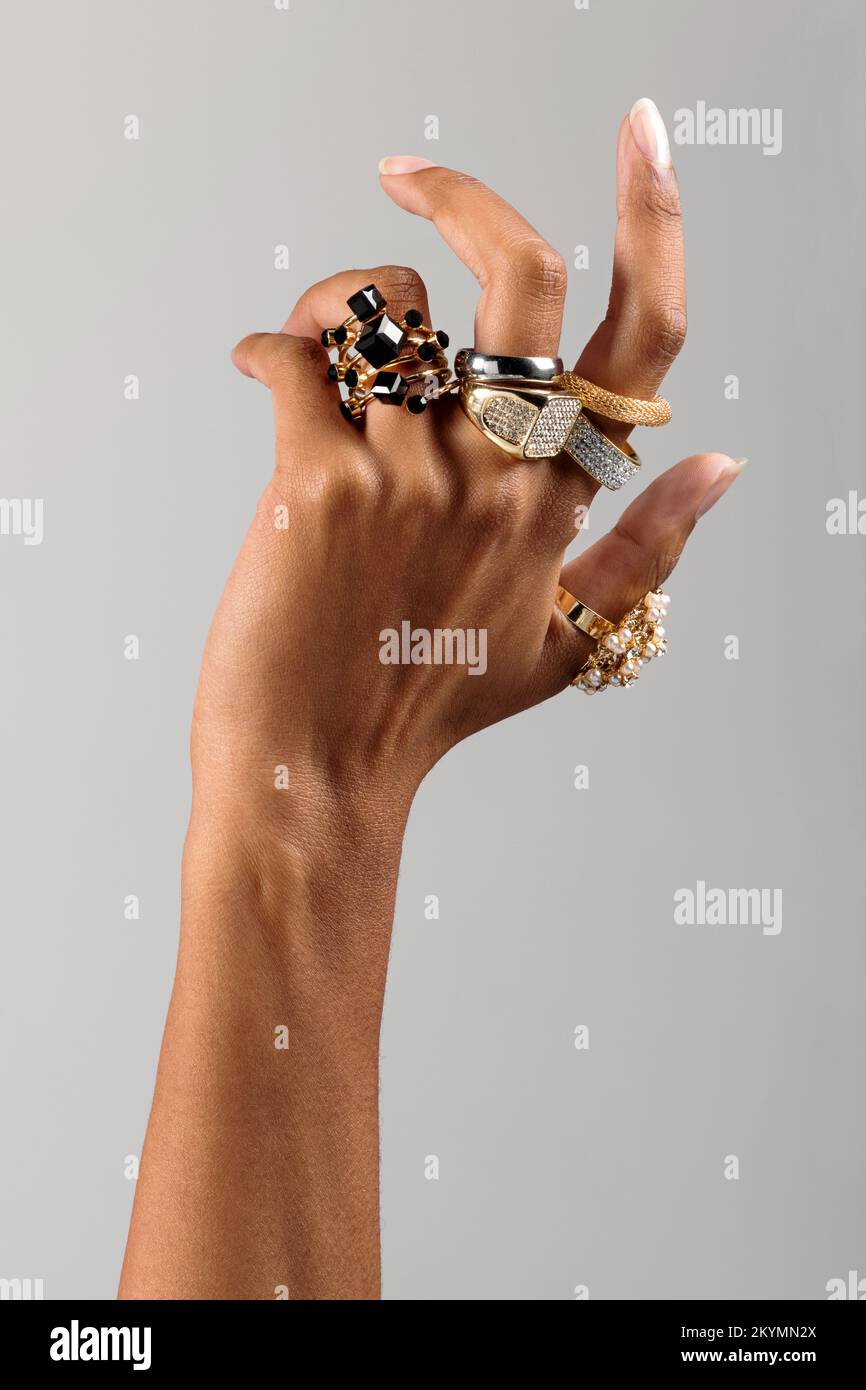 Mano de la mujer africana americana anónima usando surtido de anillos pesados elegantes contra fondo gris Foto de stock