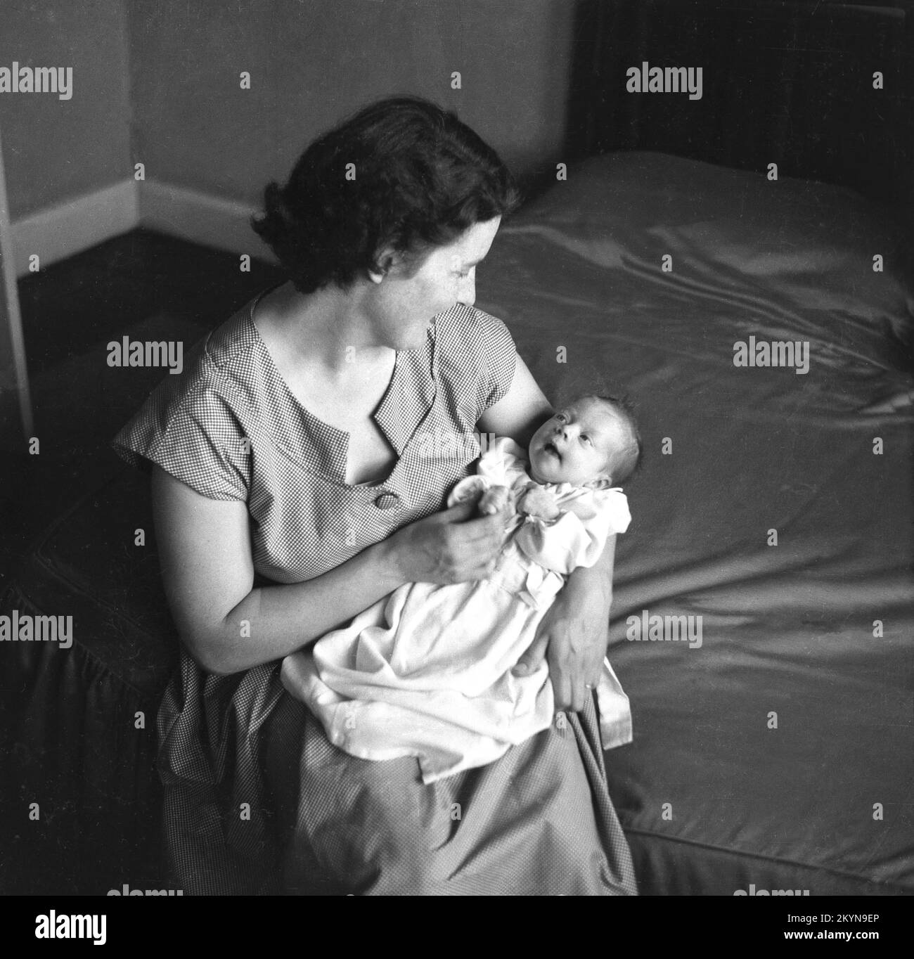 1950s, histórica, una señora sentada en el extremo de una cama, sosteniendo a su nuevo bebé, en su regazo y mirando amorosamente a sus ojos, Inglaterra, Reino Unido. Foto de stock