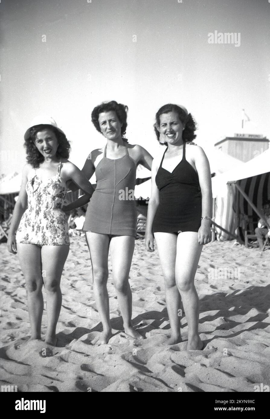 1950s, histórico, tres mujeres jóvenes en los trajes de la época de pie juntos para una foto en una playa de arena, mientras que en las vacaciones en la Europa continental. Foto de stock
