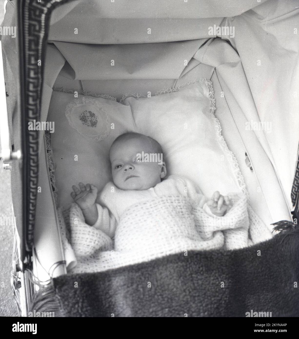 1950s, histórico, vista desde arriba de un bebé tumbado de espaldas sobre una almohada suave dentro de un cochecito construido en un autobús, con una manta de algodón a la luz y techo plegable del cochecito, Inglaterra, Reino Unido. Foto de stock