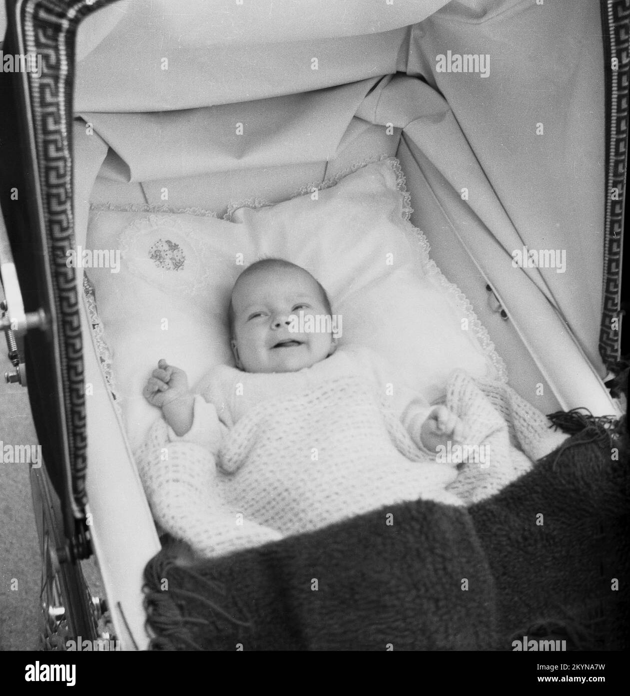 1950s, histórico, vista desde arriba de un bebé tumbado sobre la espalda en una almohada suave dentro de un cochecito construido en un autobús, con una manta de algodón a la luz y el techo plegable del cochecito, Inglaterra, Reino Unido. Foto de stock