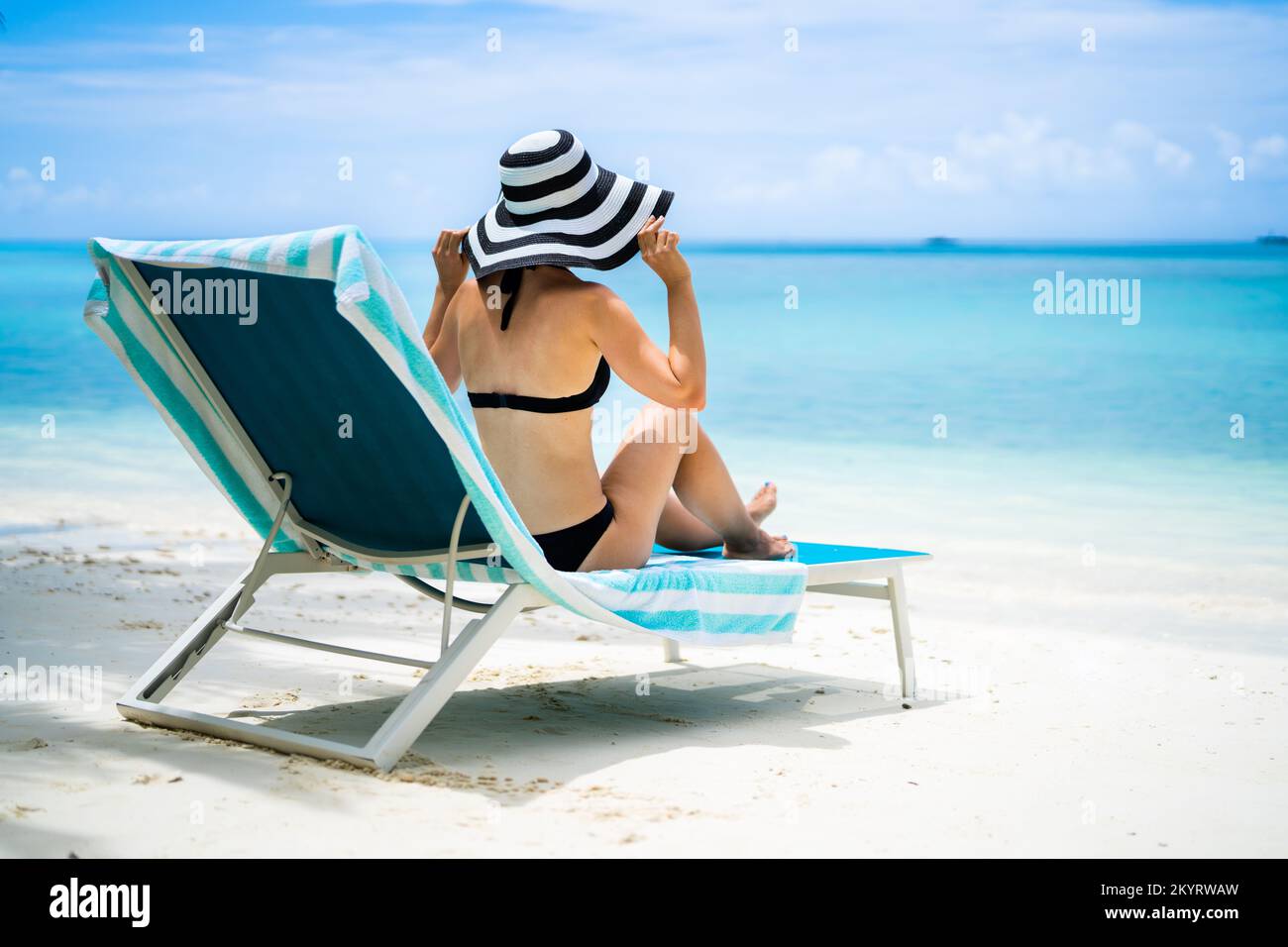 Mujer joven en Bikini tomando el sol en la silla de la cubierta en la playa Foto de stock