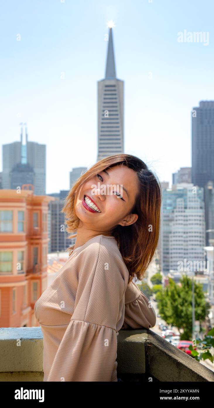 Retrato de medio cuerpo de una joven sonriente de pie con el horizonte de San Francisco en el fondo Foto de stock