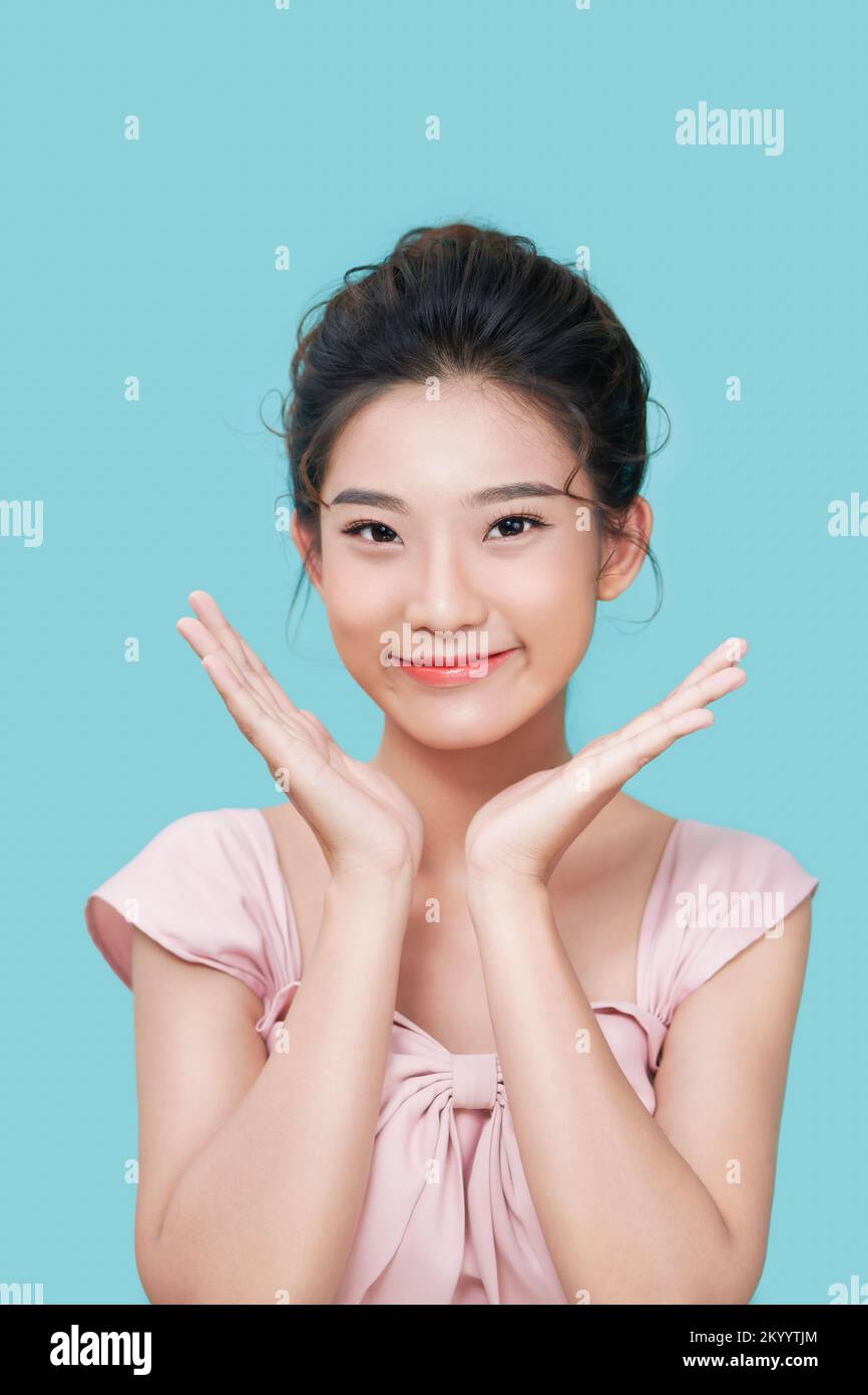 La modelo femenina asiática de aspecto agradable sonríe alegremente, extiende las palmas cerca de la cara, expresa emociones positivas aisladas sobre fondo cian Foto de stock