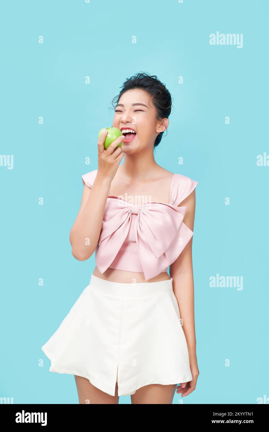 Retrato de una joven alegre comiendo manzana verde aislada sobre fondo azul Foto de stock