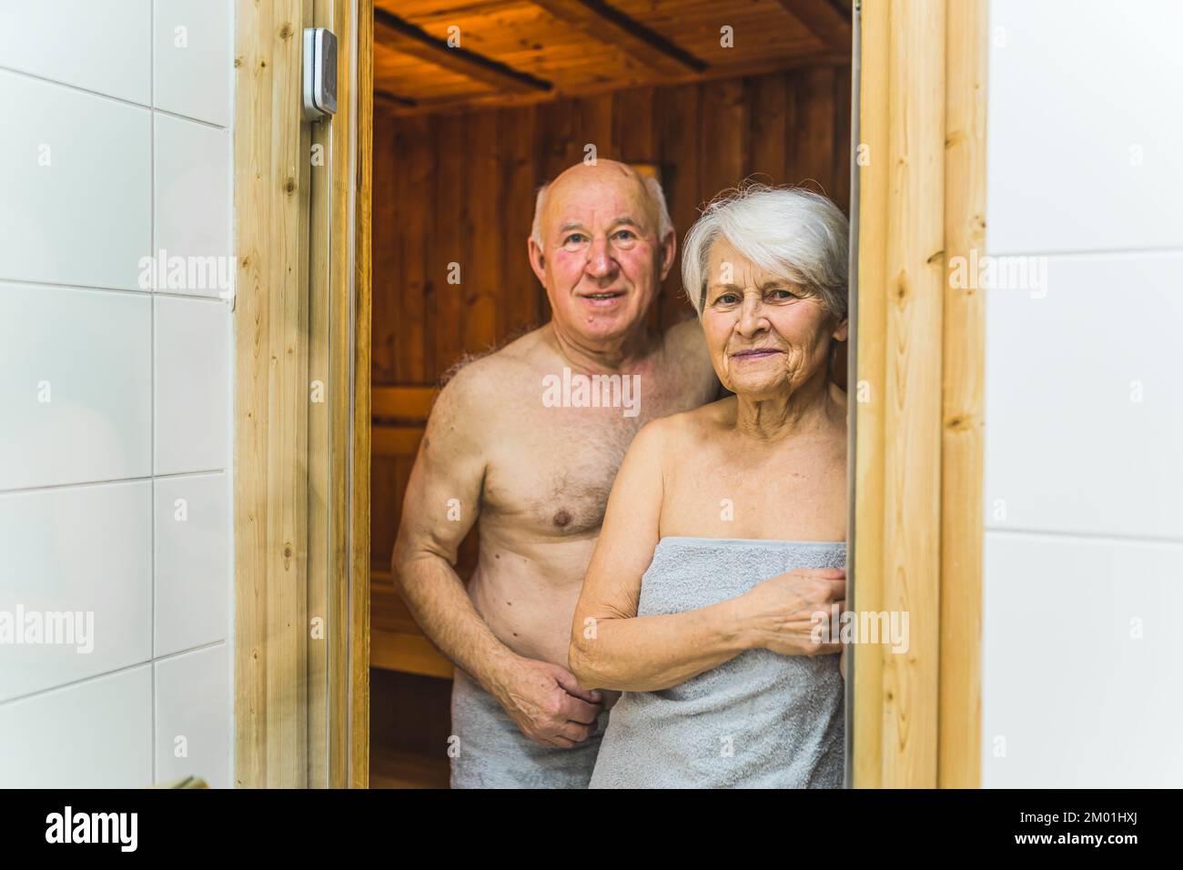 Primer plano medio en interiores de una pareja de adultos mayores caucásicos que se encuentran juntos en la entrada de la sauna de madera y miran a la cámara. . Fotografía de alta calidad Foto de stock