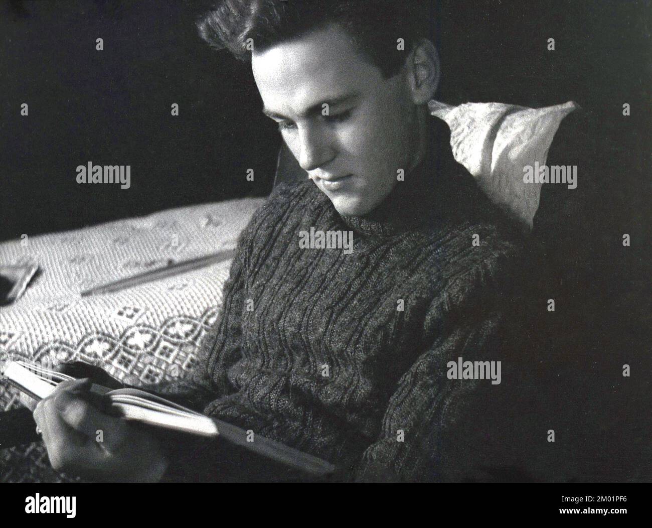 1940s, histórico, hombre joven, usando un suéter de lana de punto grueso, cuello enrollado, como usado por marinero, sentado en una silla de salón de madera armada, leyendo un libro Inglaterra, Reino Unido. Foto de stock