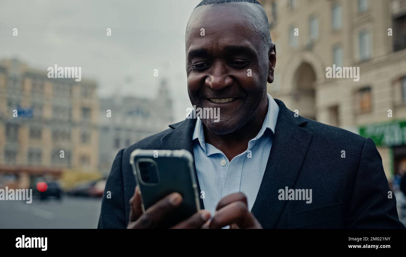Mediana edad empresario africano hombre étnico trabajador empleador empresario en la ciudad al aire libre mirando el teléfono móvil mediante el servicio público de navegación Wi-Fi Foto de stock